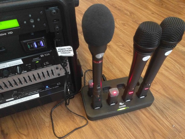 A close-up view of the Revolabs microphone charger with five microphones inserted and power indicators lit