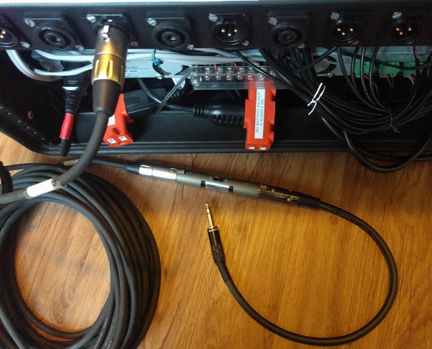 The rear of the rack case with a long XLR cable, a signal attenuator, and a short XLR/TRS adapter cable